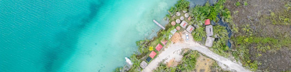 An aerial view of a coastal area with turquoise waters, a sandy beach, and several small structures with red roofs.