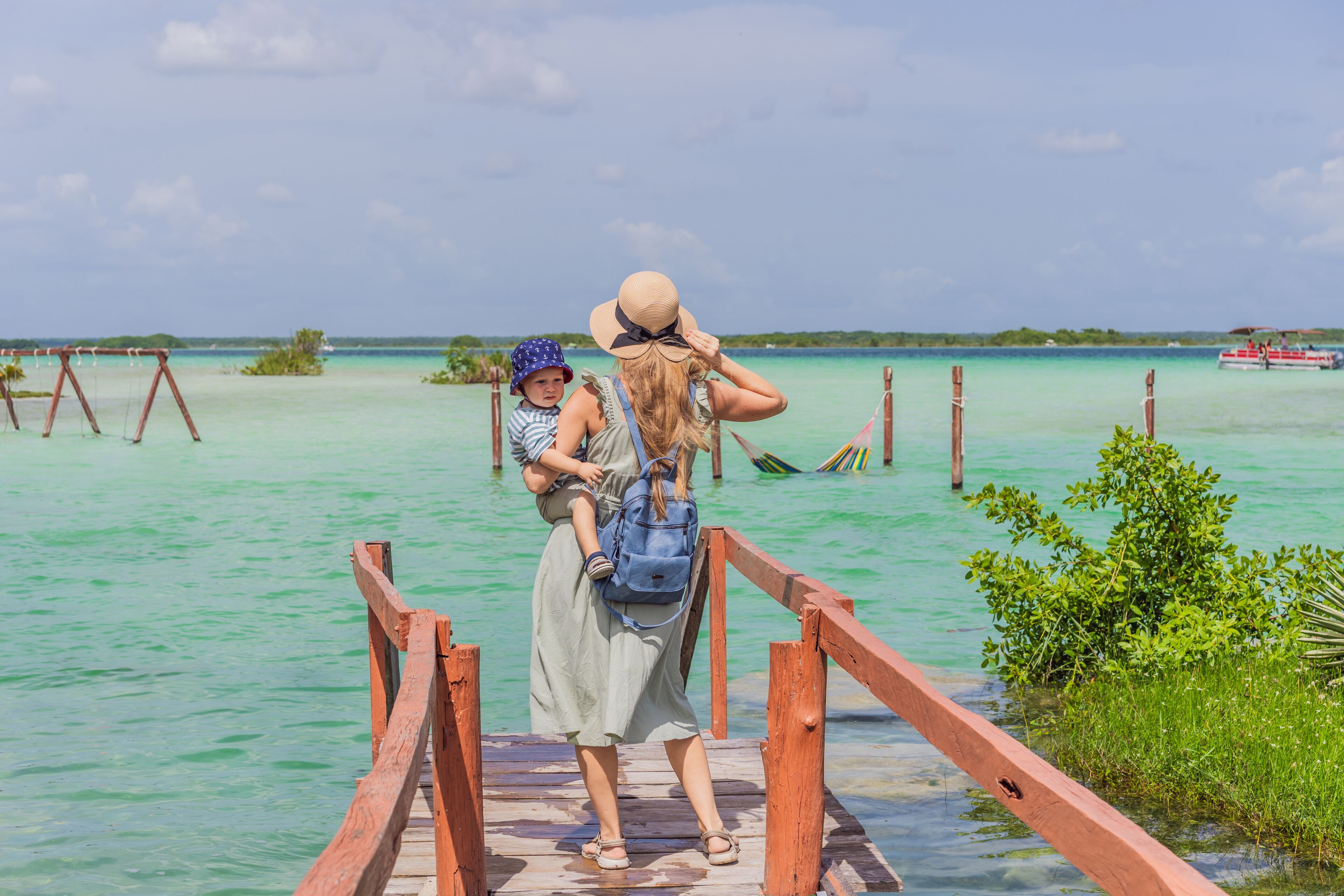 Mother with his toddler son exploring wooden pier over the turquoise waters of Bacalar Lake, Mexico. Peaceful tropical travel destination concept