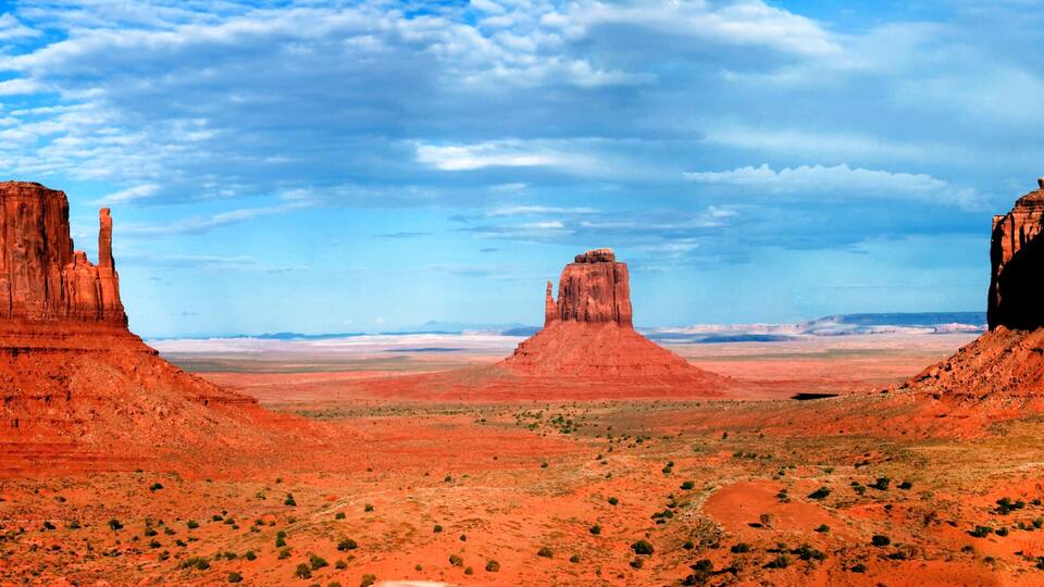Three red rock formations in a desert landscape with a clear sky.