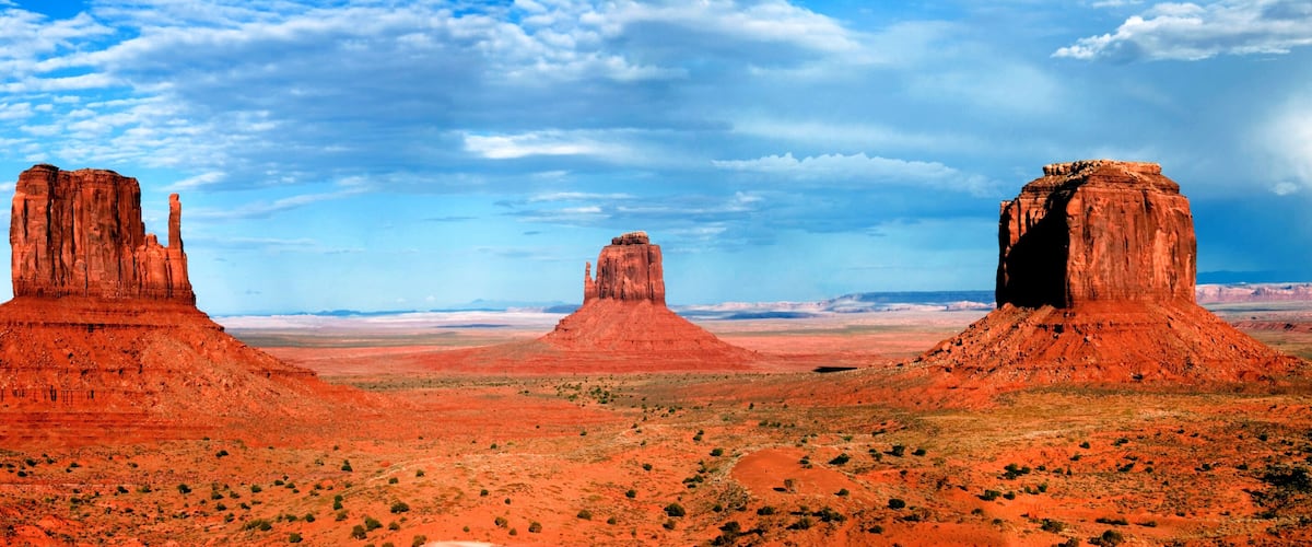 Three red rock formations in a desert landscape with a clear sky.