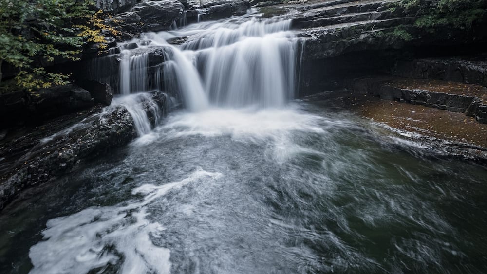 Une cascade d’eau qui dévale des rochers dans une zone boisée.