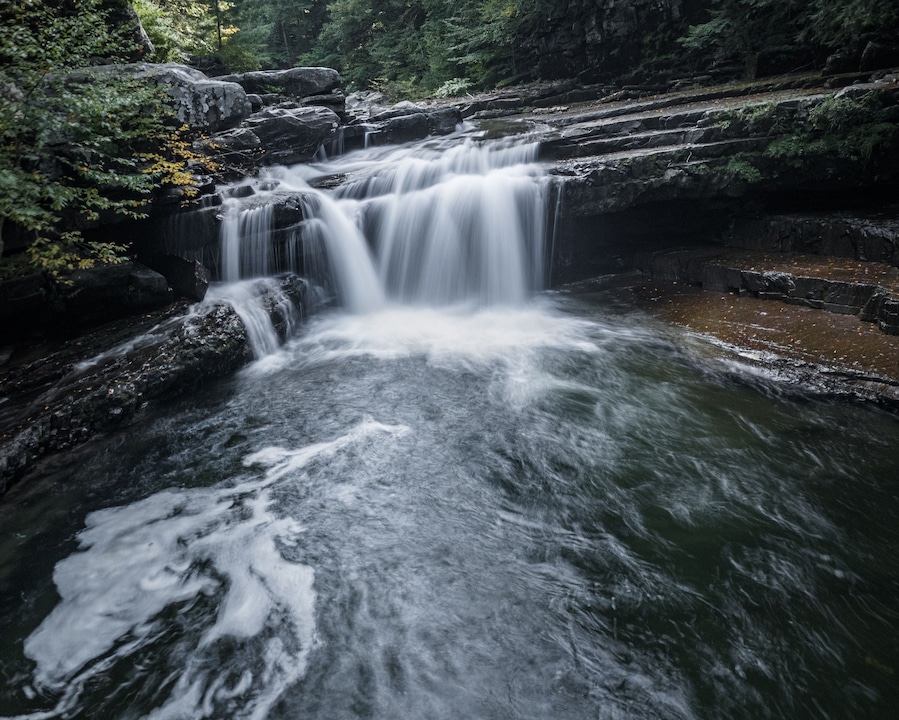 Una cascada fluye sobre rocas en un área boscosa.