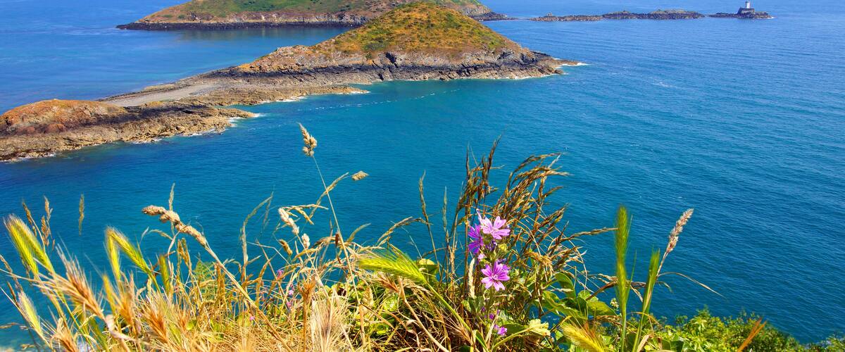 A coastal landscape with rocky outcrops and a lighthouse in the distance.