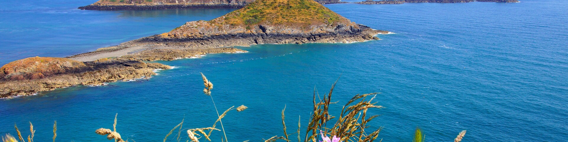 A coastal landscape with rocky outcrops and a lighthouse in the distance.