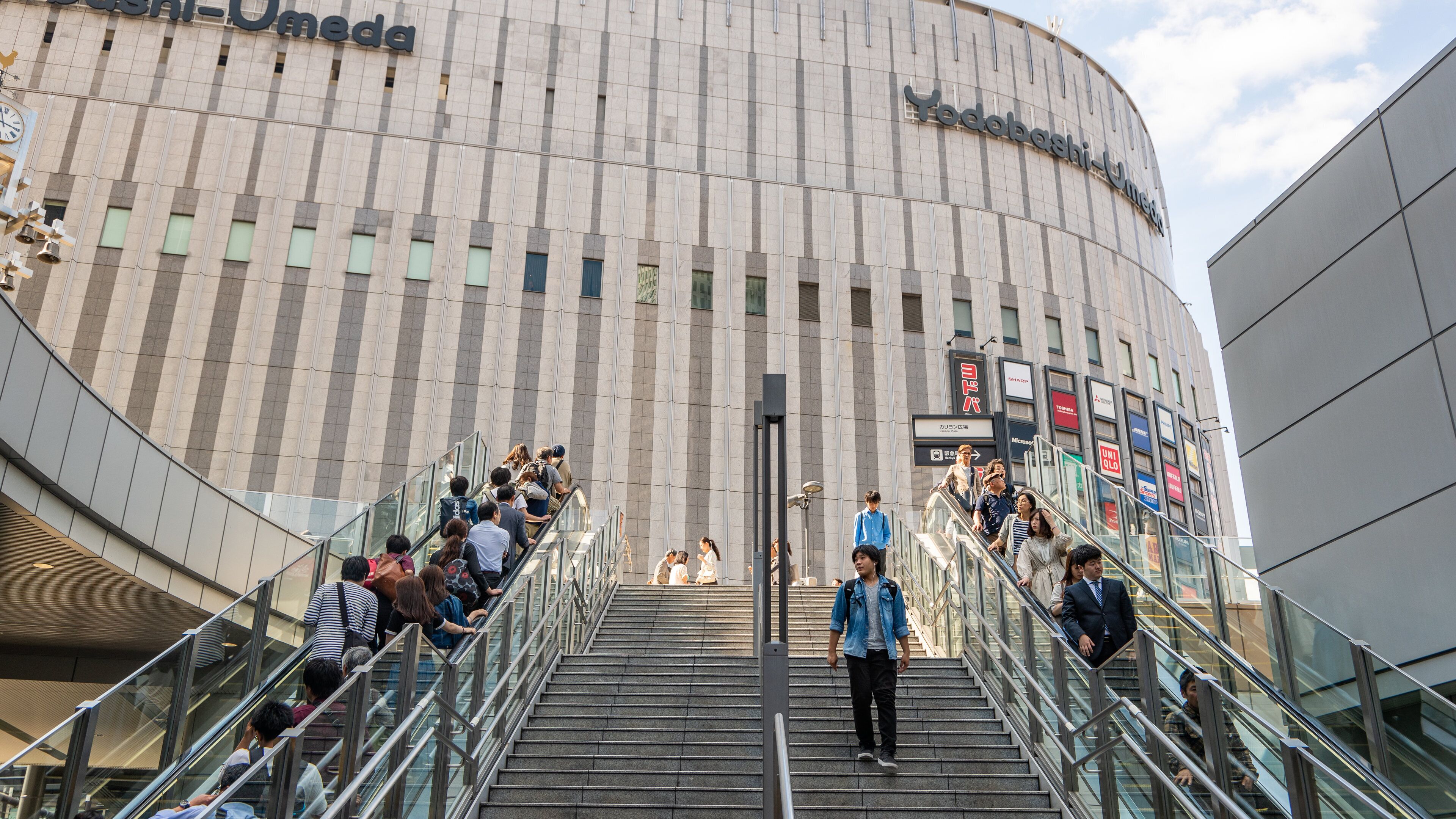 Un edifici modern amb façana corbada i diversos rèstols, incloent-hi 'Yodobashi-Umeda'.