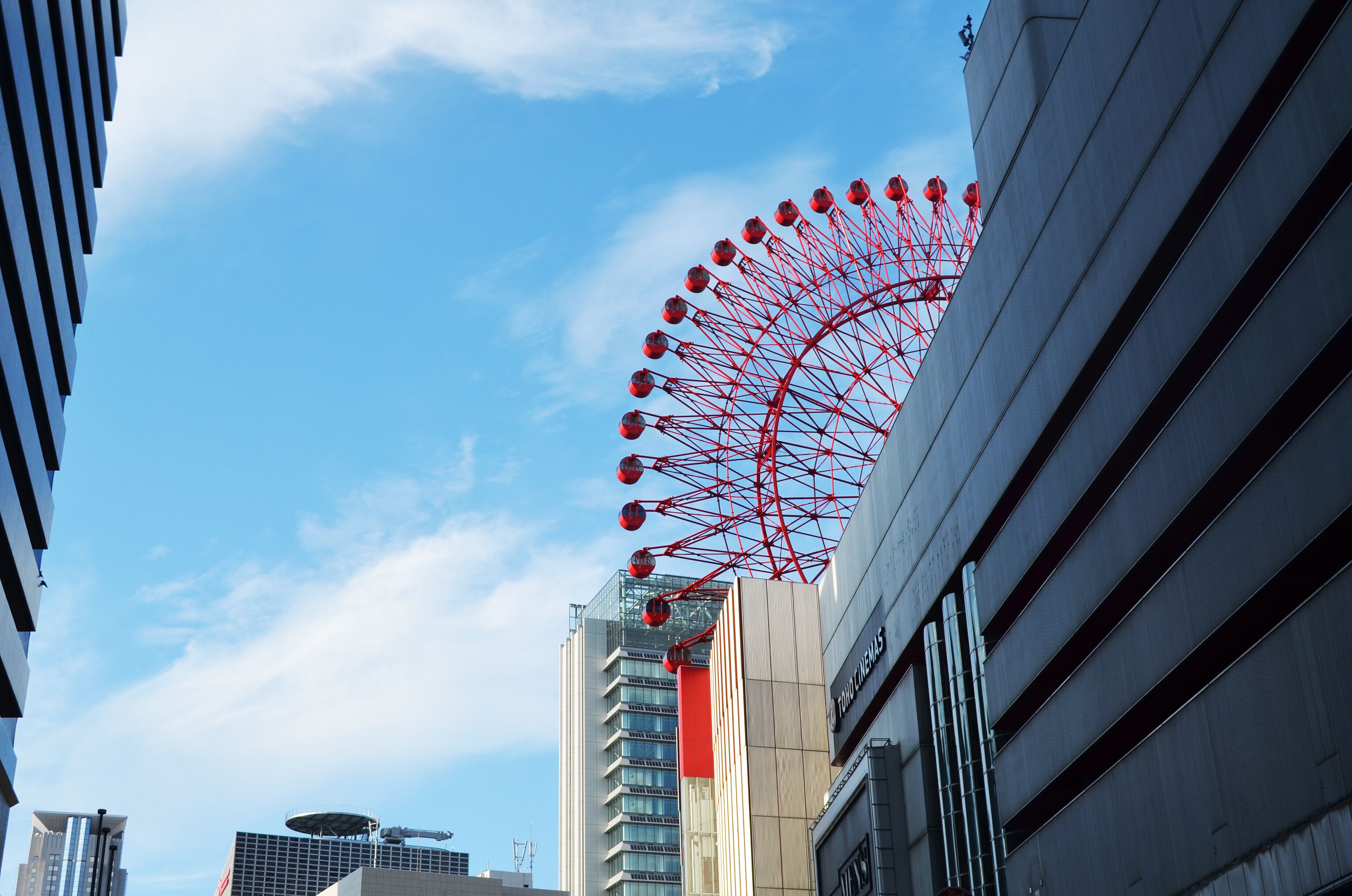 A Ferris wheel against a clear blue sky, with modern buildings in the foreground.