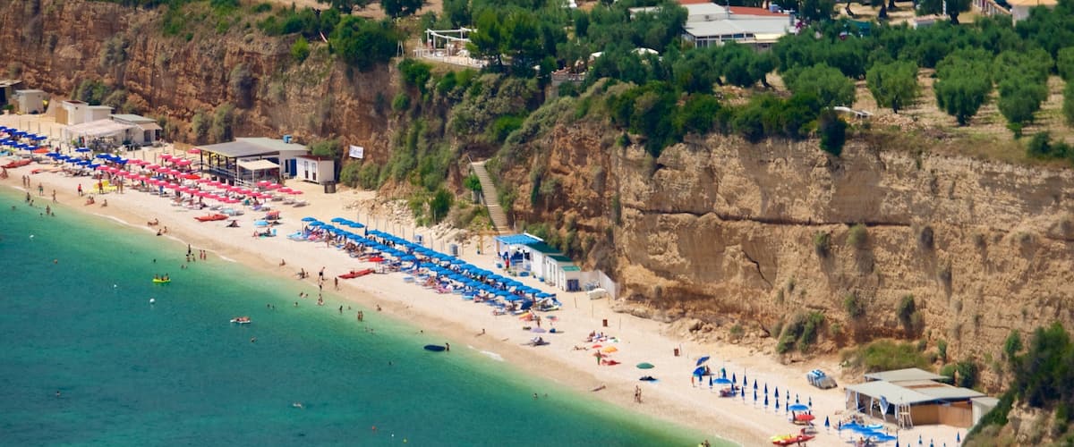 A coastal beach with clear turquoise waters, a sandy shore, and a rocky cliff.