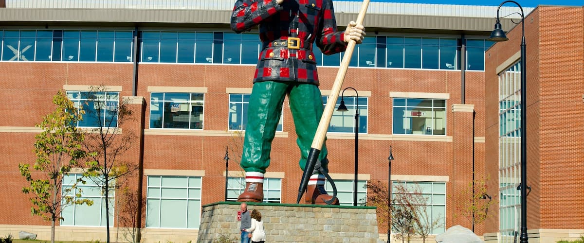 A large outdoor statue of a man holding a shovel and a pickaxe in front of a brick building with large windows.
