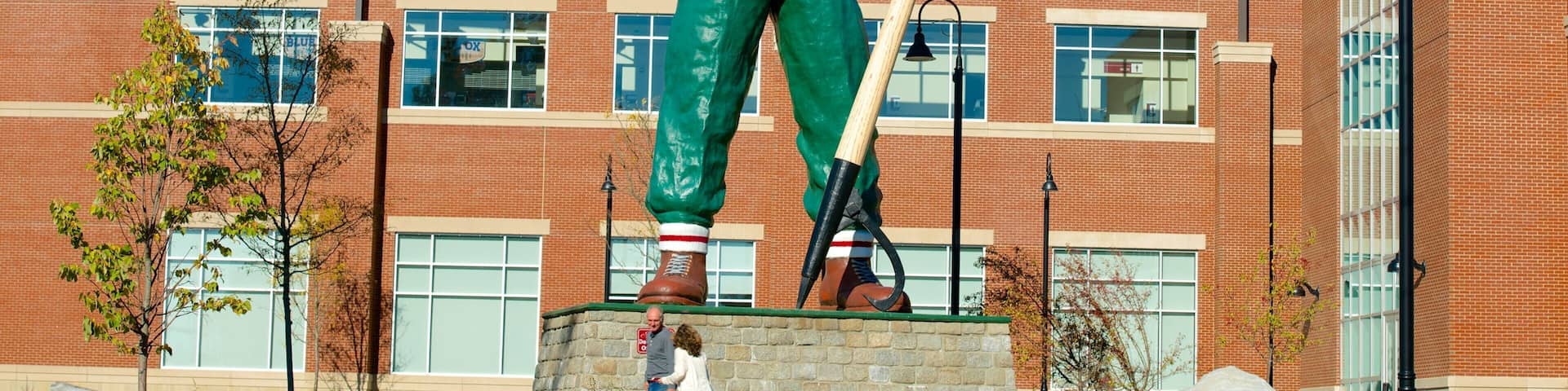 A large outdoor statue of a man holding a shovel and a pickaxe in front of a brick building with large windows.