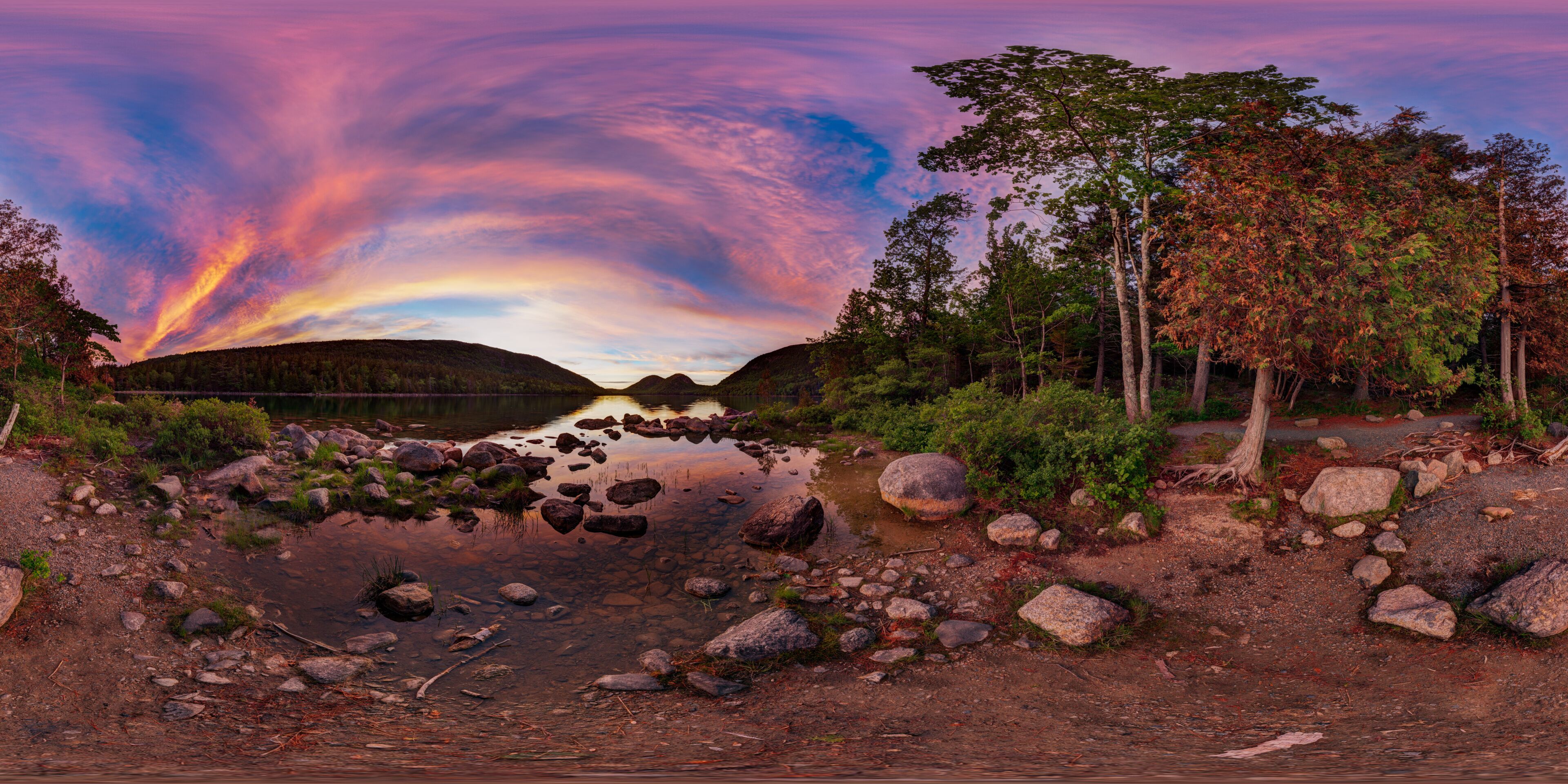 A river with rocks and trees, a mountain in the background, and a colorful sky.