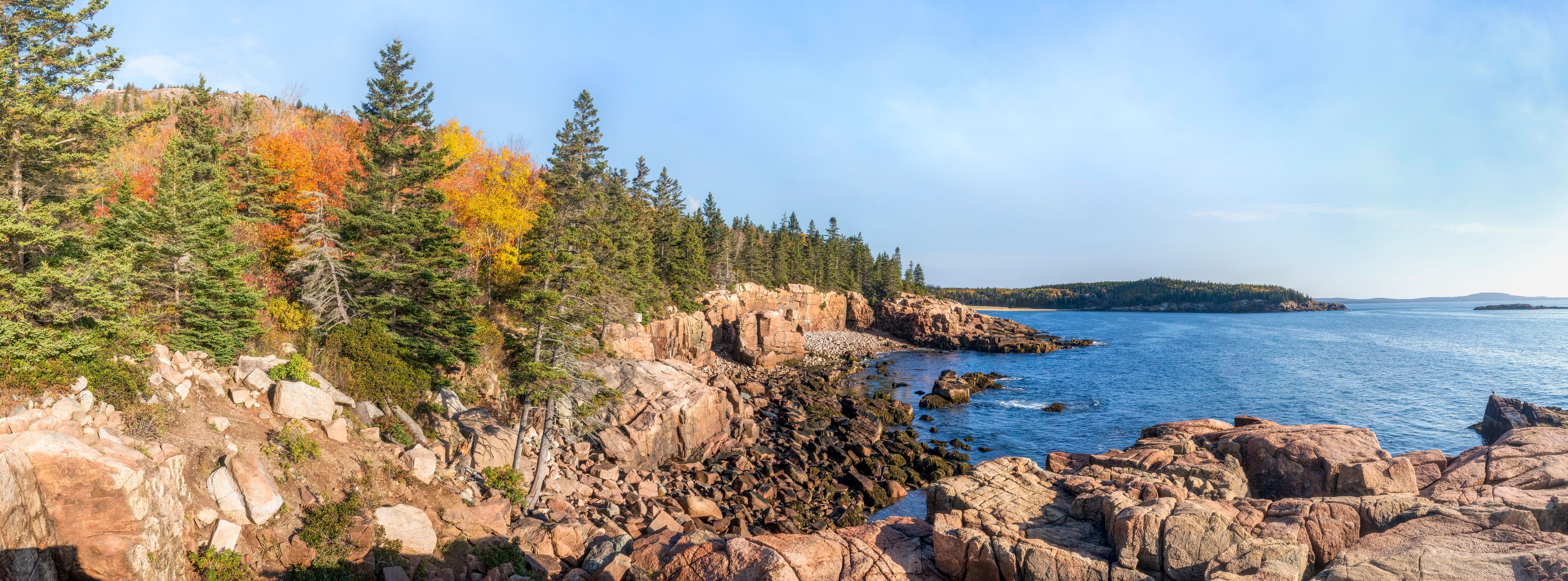 A coastal landscape with rocky cliffs, autumn-colored trees, and a calm sea.