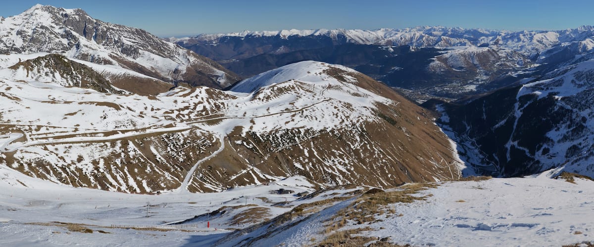 A snow-covered mountain range with a winding road and ski tracks.