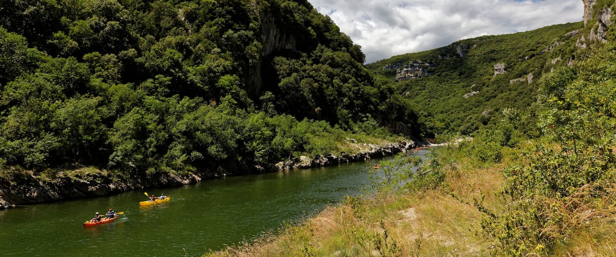 A river with kayaks, surrounded by lush green hills and a clear sky.