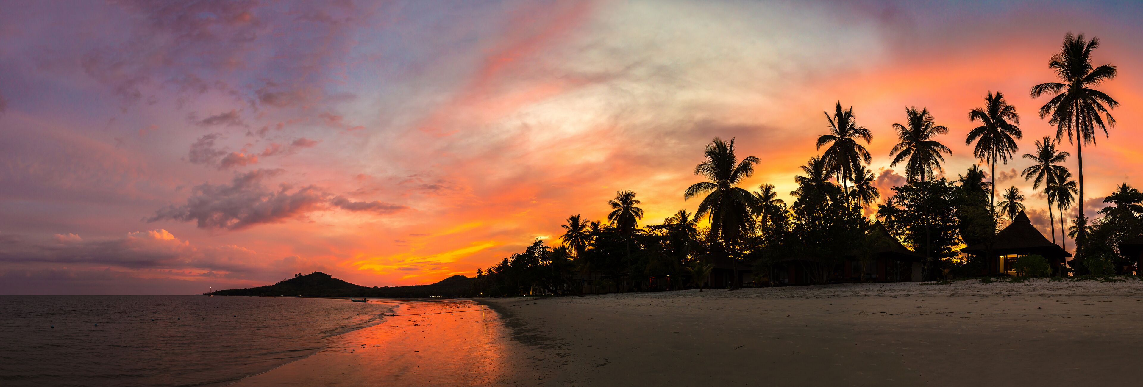 A beach at sunset with palm trees and a small hut.