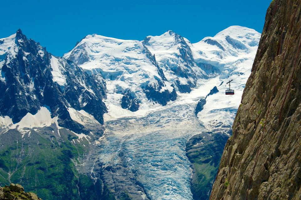 A glacier with snow-covered mountains in the background and a cable car in the midground.