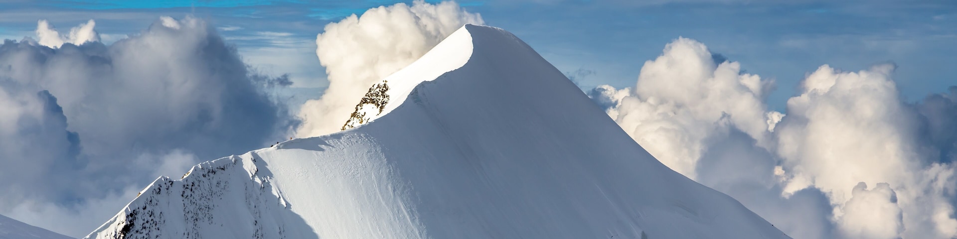 A snow-covered mountain peak with a clear sky and clouds in the background.