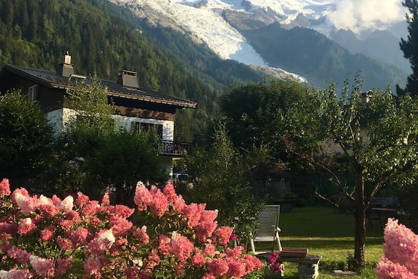 Un paysage de montagne avec des sommets enneigés, une maison et, au premier plan, des fleurs roses en pleine floraison.