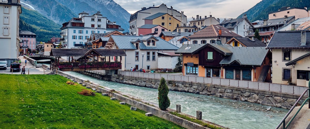 A riverside town with historic buildings, a river, and snow-capped mountains in the background.
