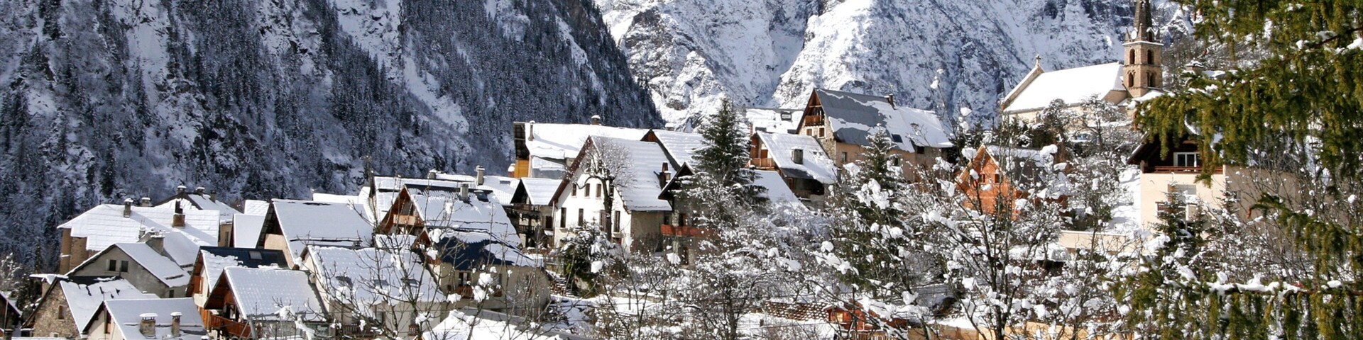 A snow-covered village with traditional wooden houses and a church, surrounded by snow-capped mountains.