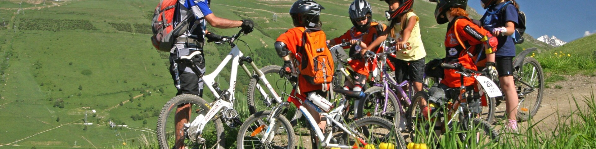 Um grupo de ciclistas de montanha em uma trilha, com montanhas ao fundo.