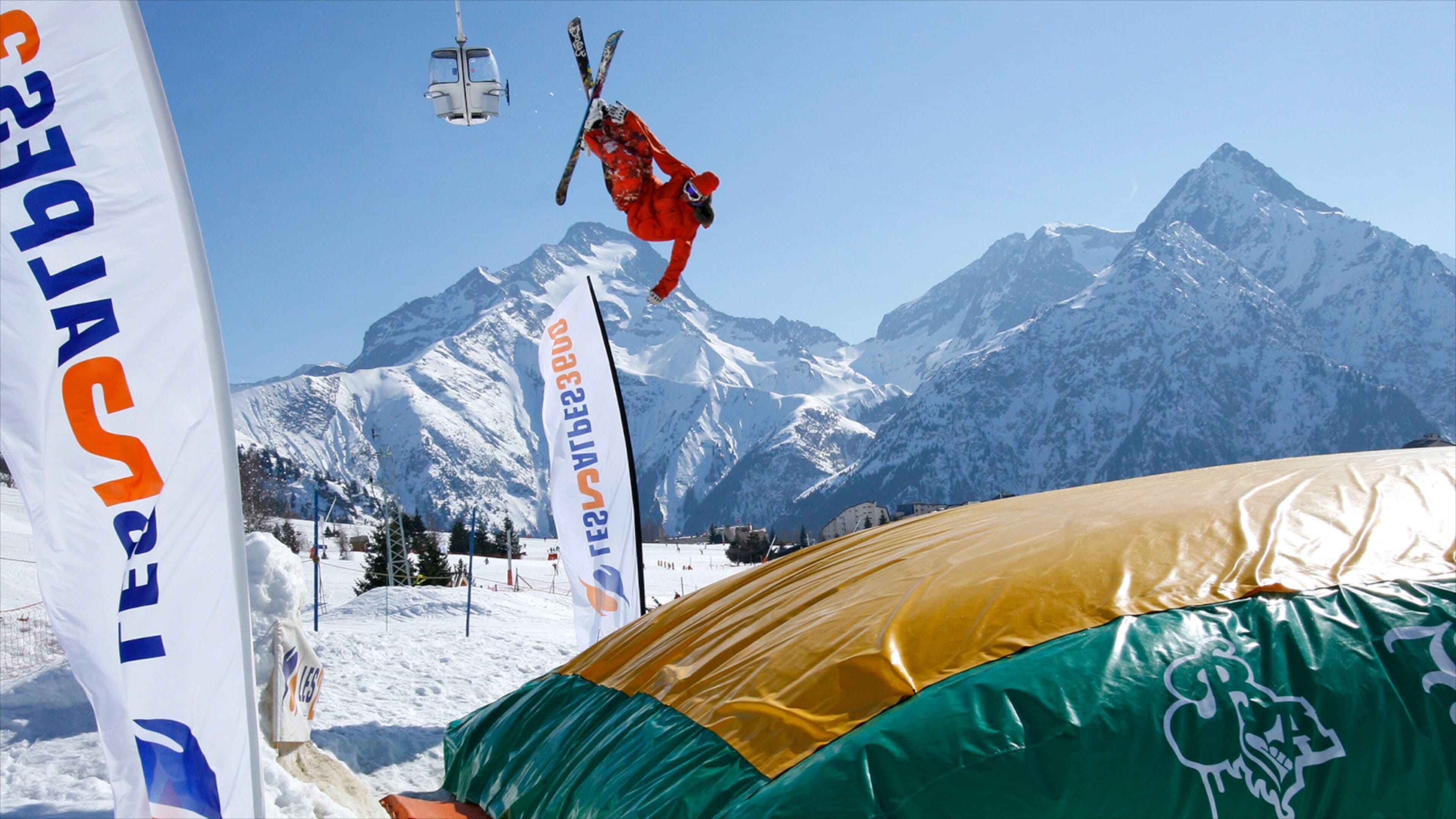 A skier performing a trick in mid-air with a mountainous backdrop.