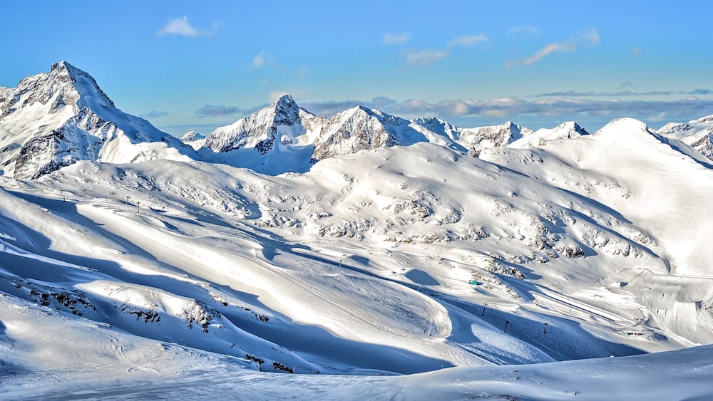 A snow-covered mountain range with sharp peaks and winding ski trails.