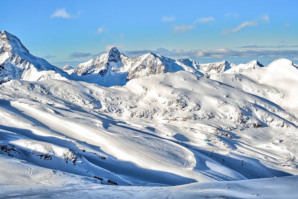 A snow-covered mountain range with sharp peaks and winding ski trails.