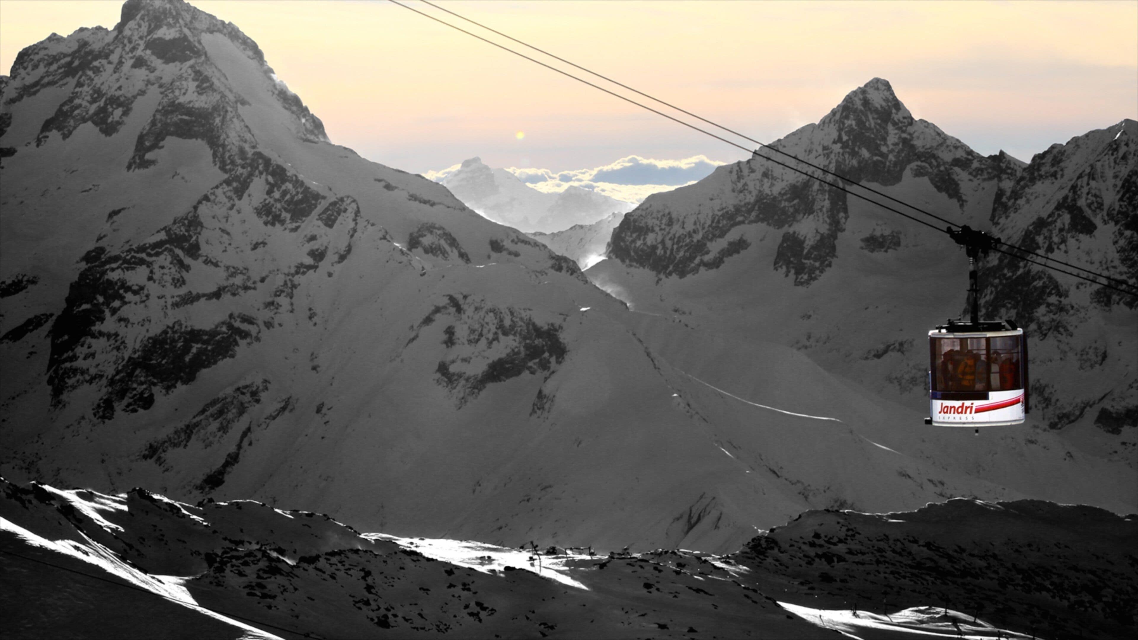 A cable car in a mountainous landscape with snow-covered peaks and a clear sky.