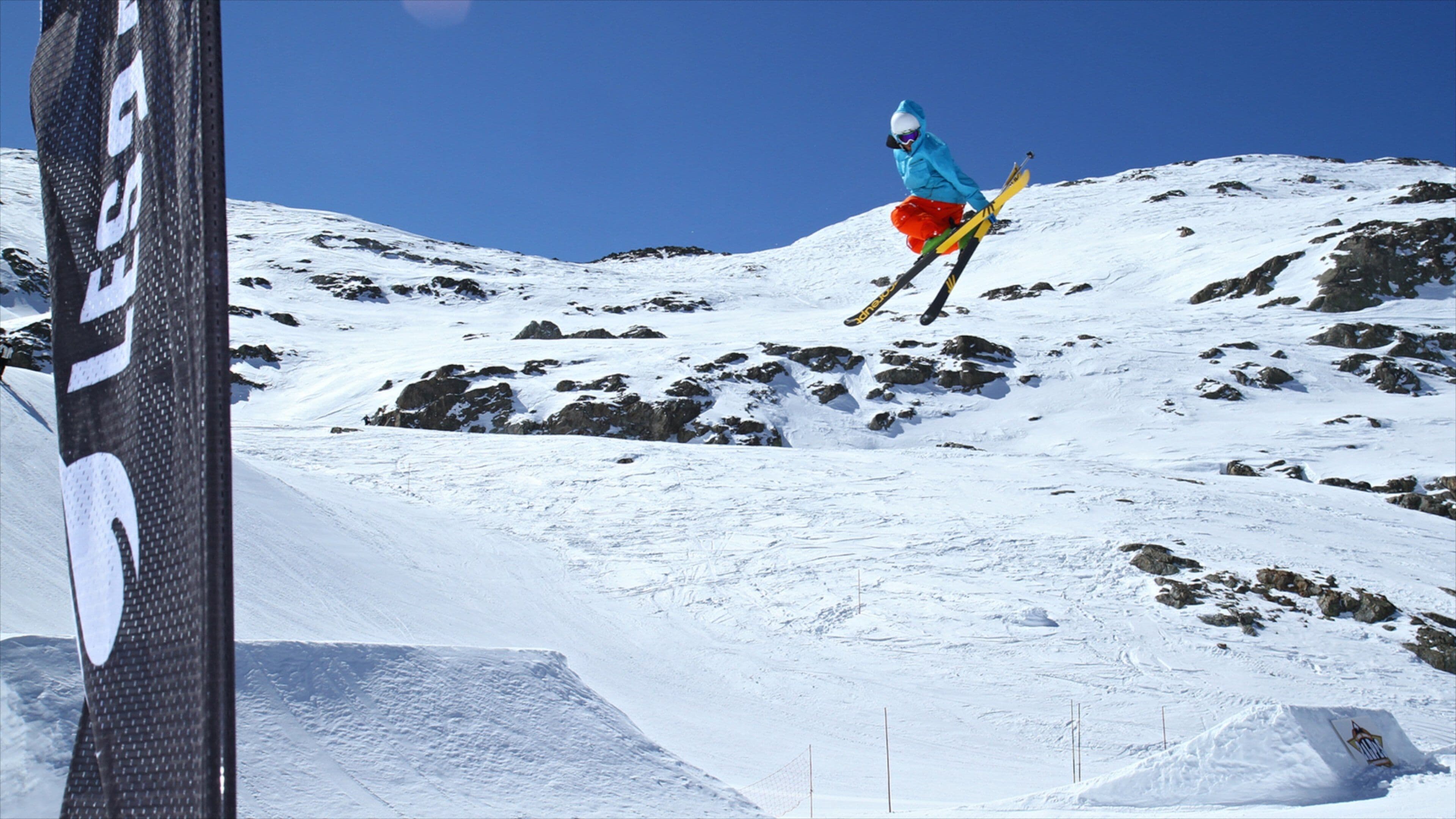 Ein Skifahrer in der Luft, der eine Sprungvorbereitung auf einem verschneiten Berghang macht.