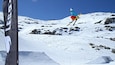 Ein Skifahrer in der Luft, der eine Sprungvorbereitung auf einem verschneiten Berghang macht.