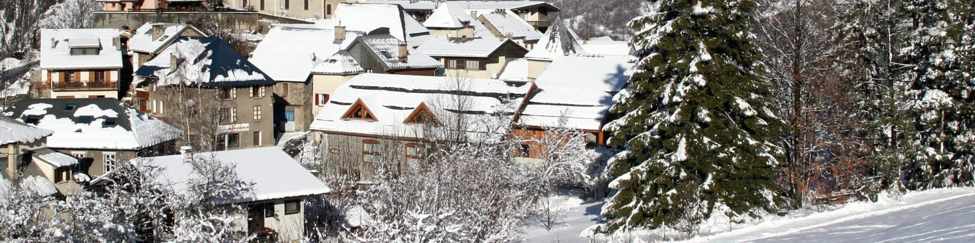 A snow-covered village with traditional buildings and a church, surrounded by snow-capped mountains.