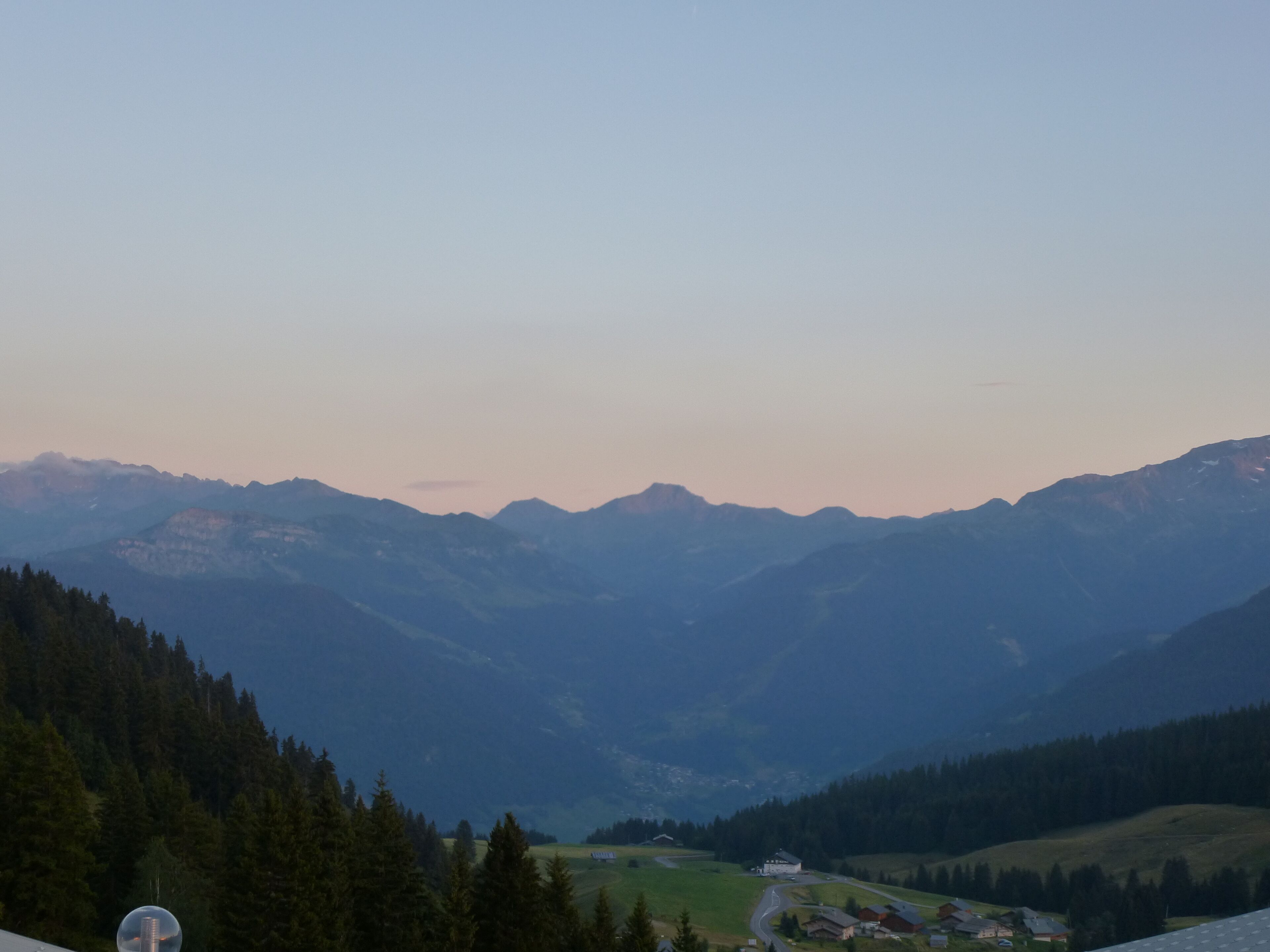 A mountainous landscape with a valley, forested areas, and a small village.
