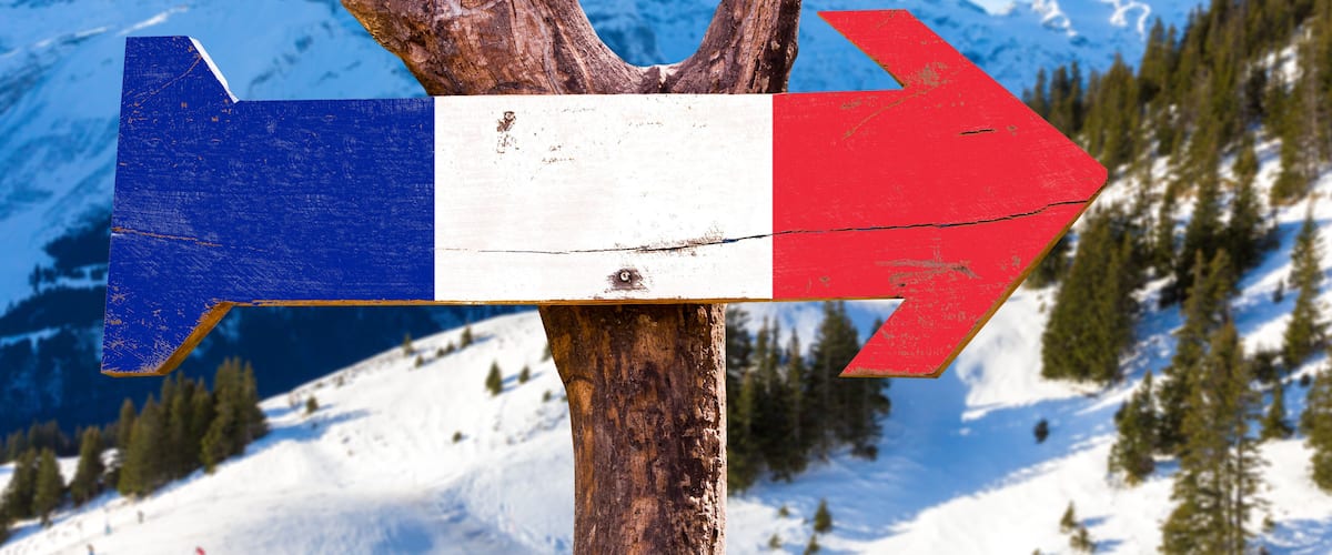 A wooden signpost with blue, white, and red directional arrows against a snowy mountain backdrop.