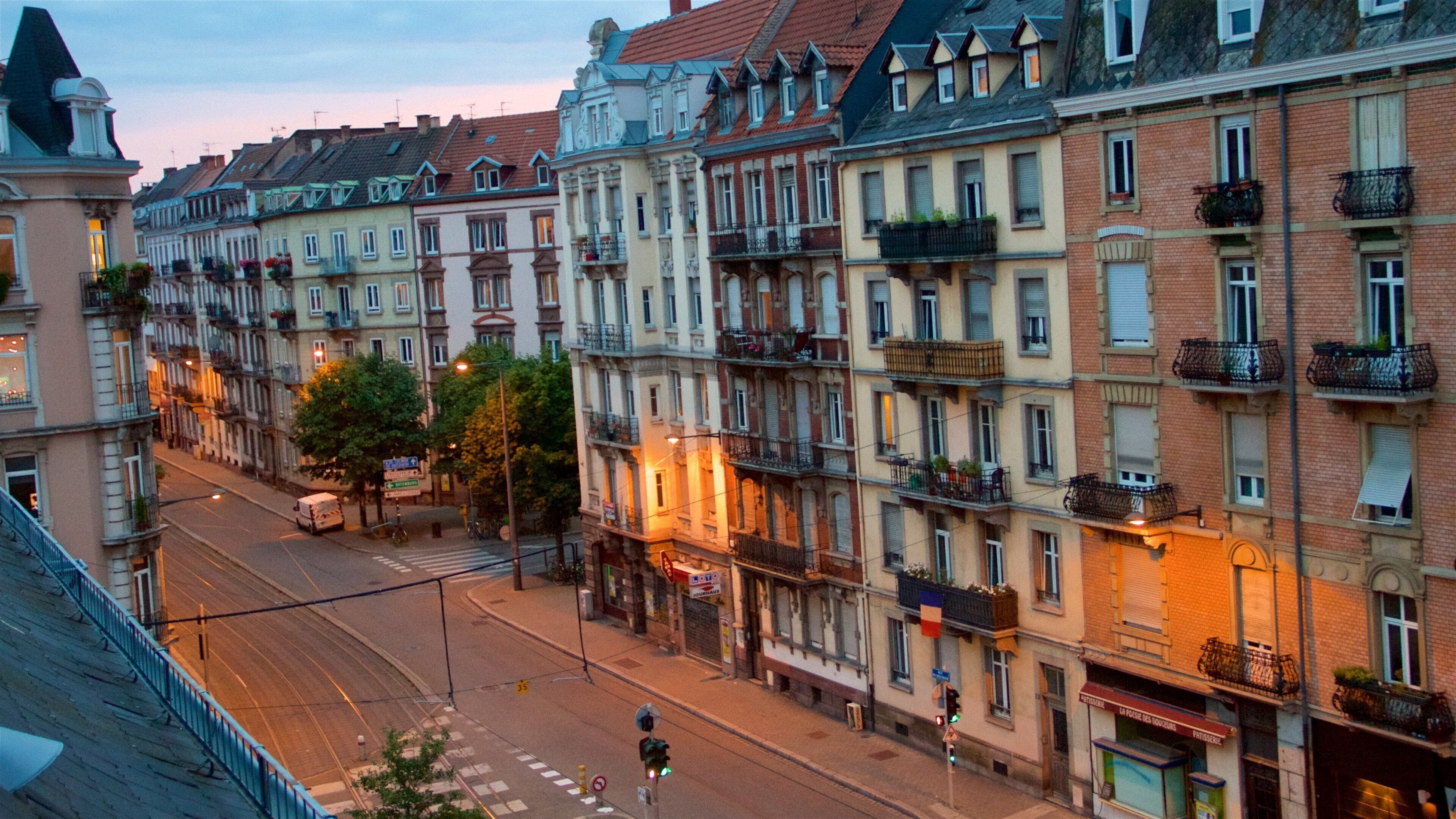 A street lined with multi-story buildings with balconies and awnings, under a twilight sky.