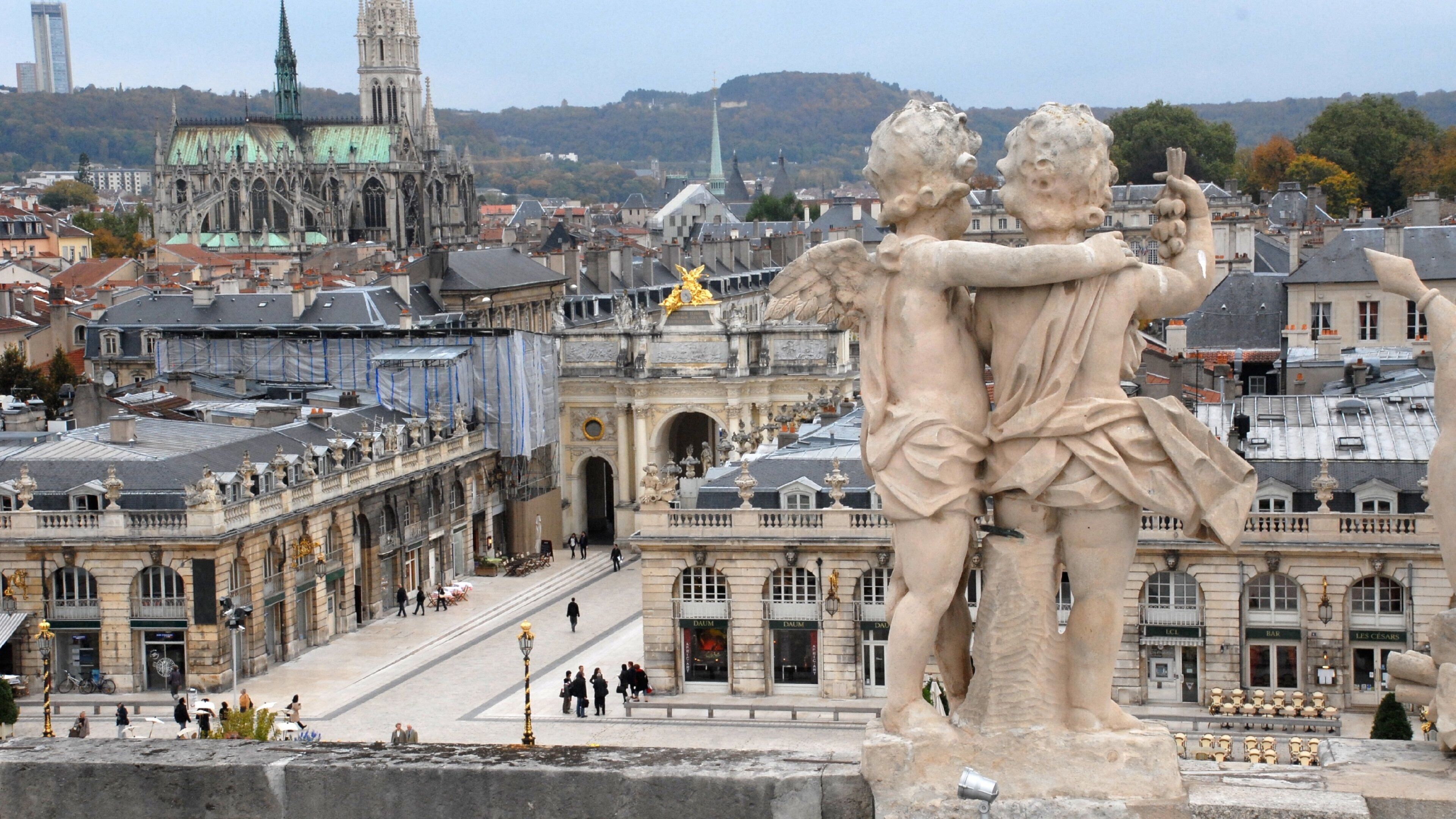 A statue of cherubs embracing, a historic building with arches, and a cathedral in the background.