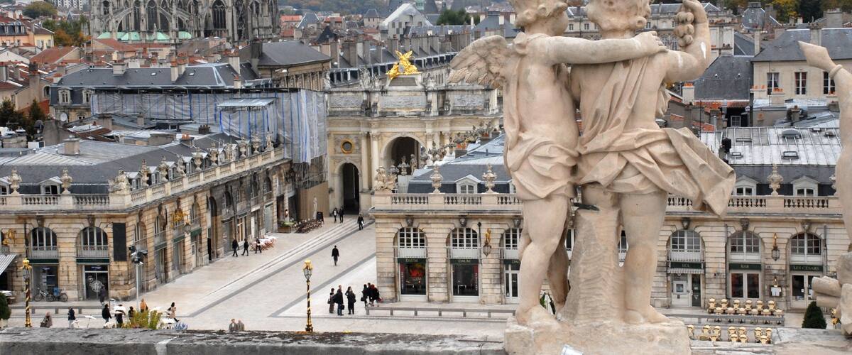 A statue of cherubs embracing, a historic building with arches, and a cathedral in the background.