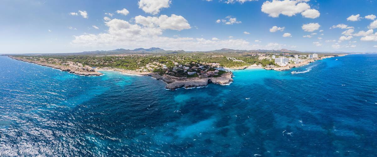 A coastal town with a rocky shoreline, clear blue waters, and a backdrop of mountains.