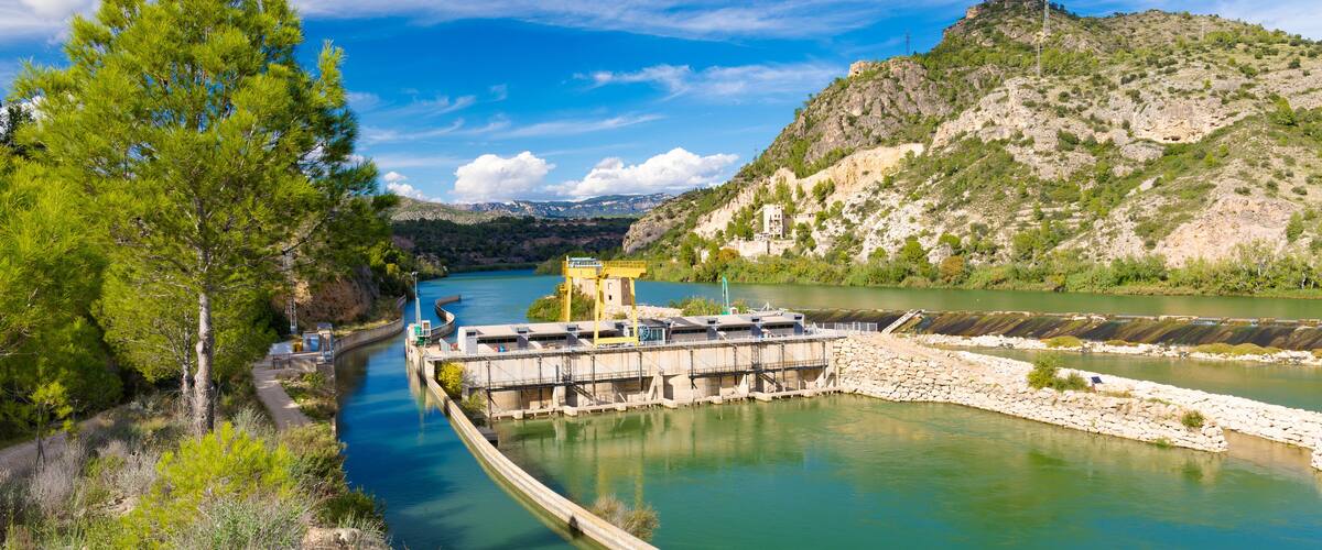A river with a dam, a bridge, and a mountainous landscape.