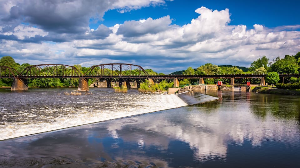 A steel bridge over a river with a dam in the foreground.