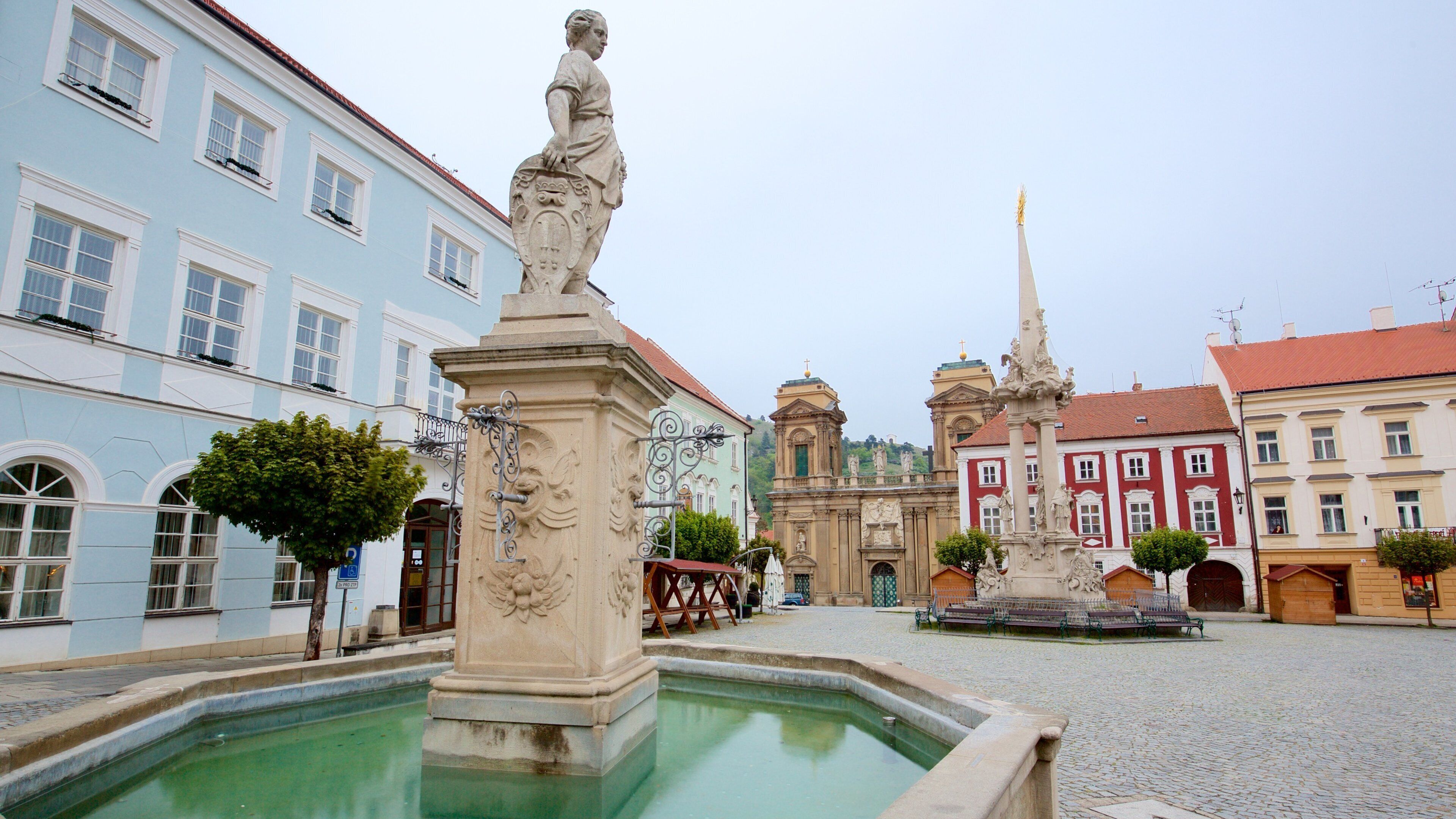 A historic square with a fountain, a statue, and classical architecture.
