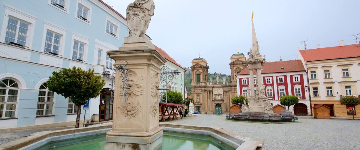 A historic square with a fountain, a statue, and classical architecture.