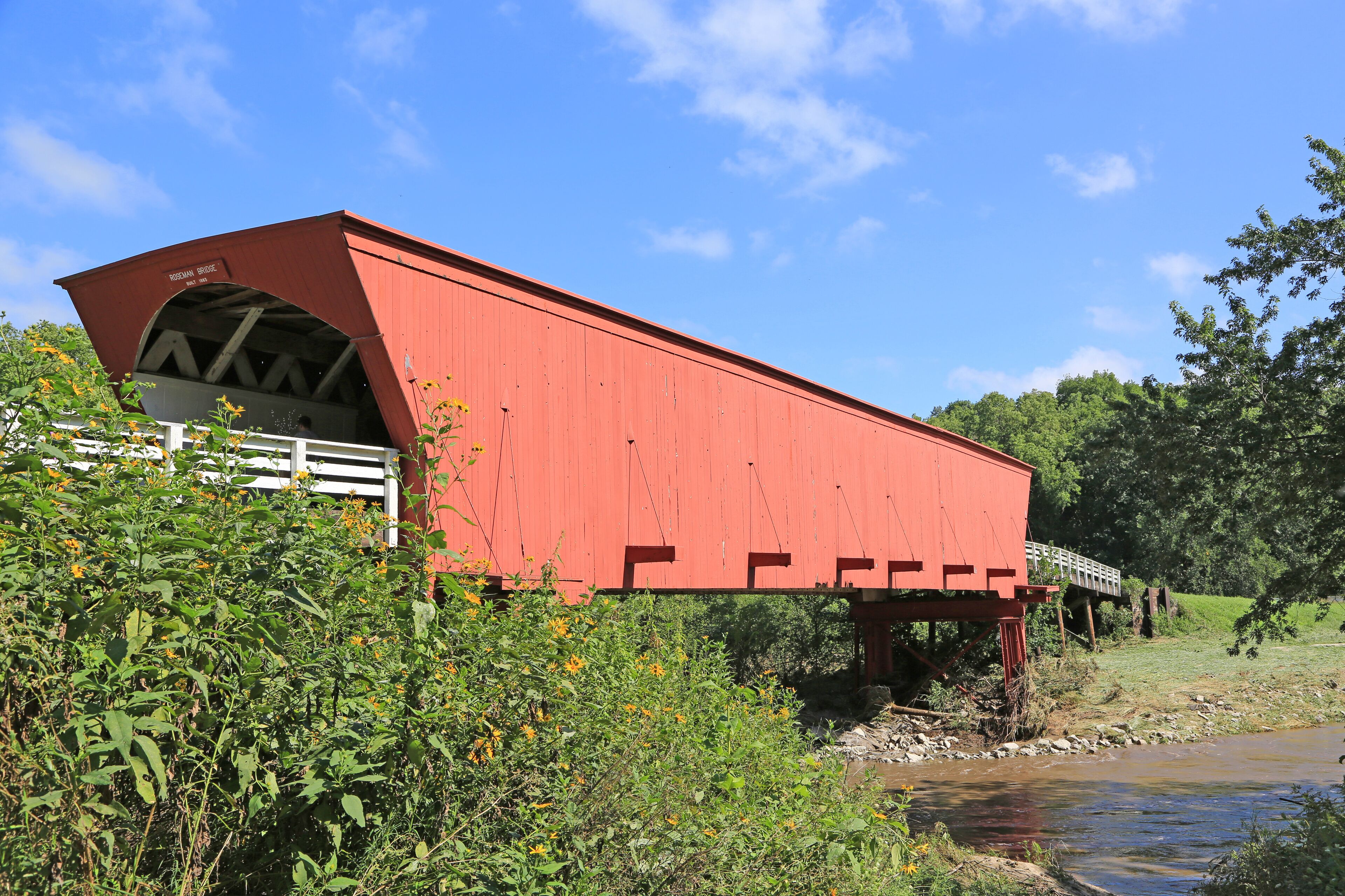 A red covered bridge over a river with greenery and a clear blue sky.