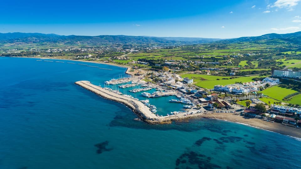 A coastal town with a marina, boats, and a mountainous backdrop.
