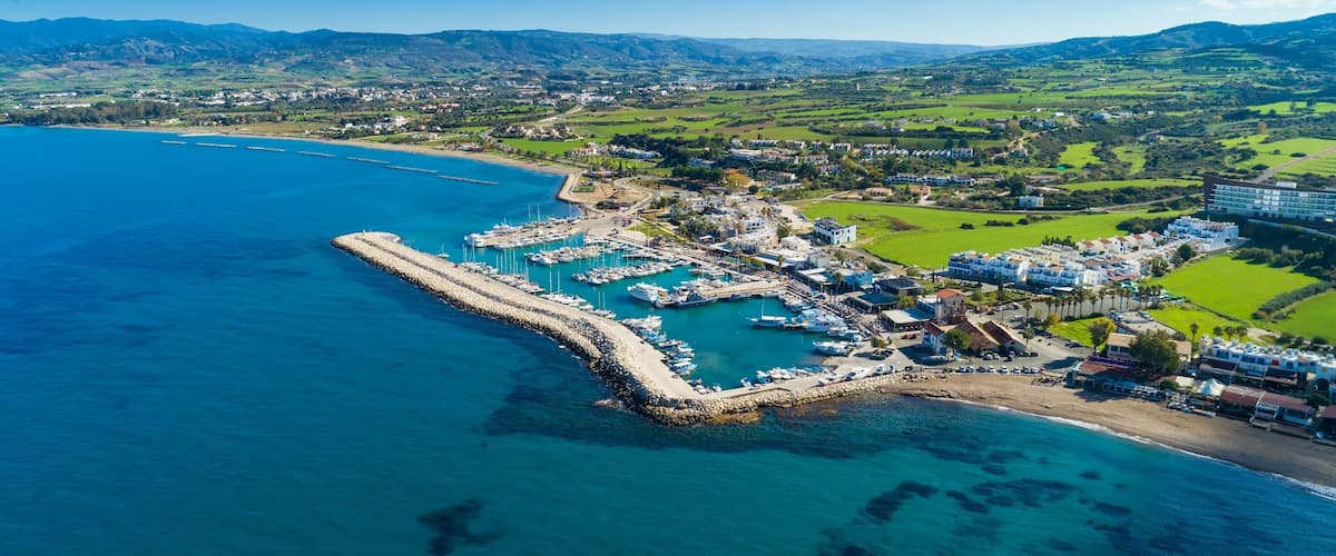 A coastal town with a marina, boats, and a mountainous backdrop.