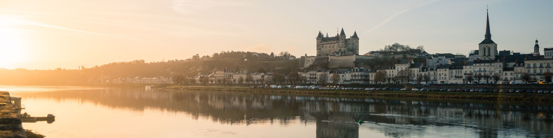 Um rio calmo refletindo uma cidade histórica com um castelo e igreja imponentes.