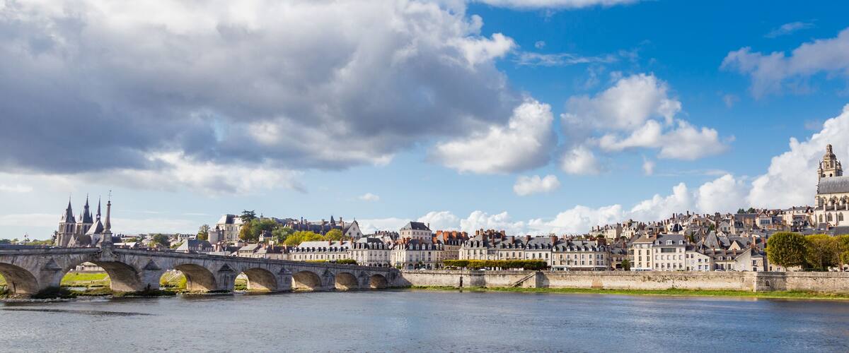 A river with a stone bridge, historic buildings, and a prominent cathedral.