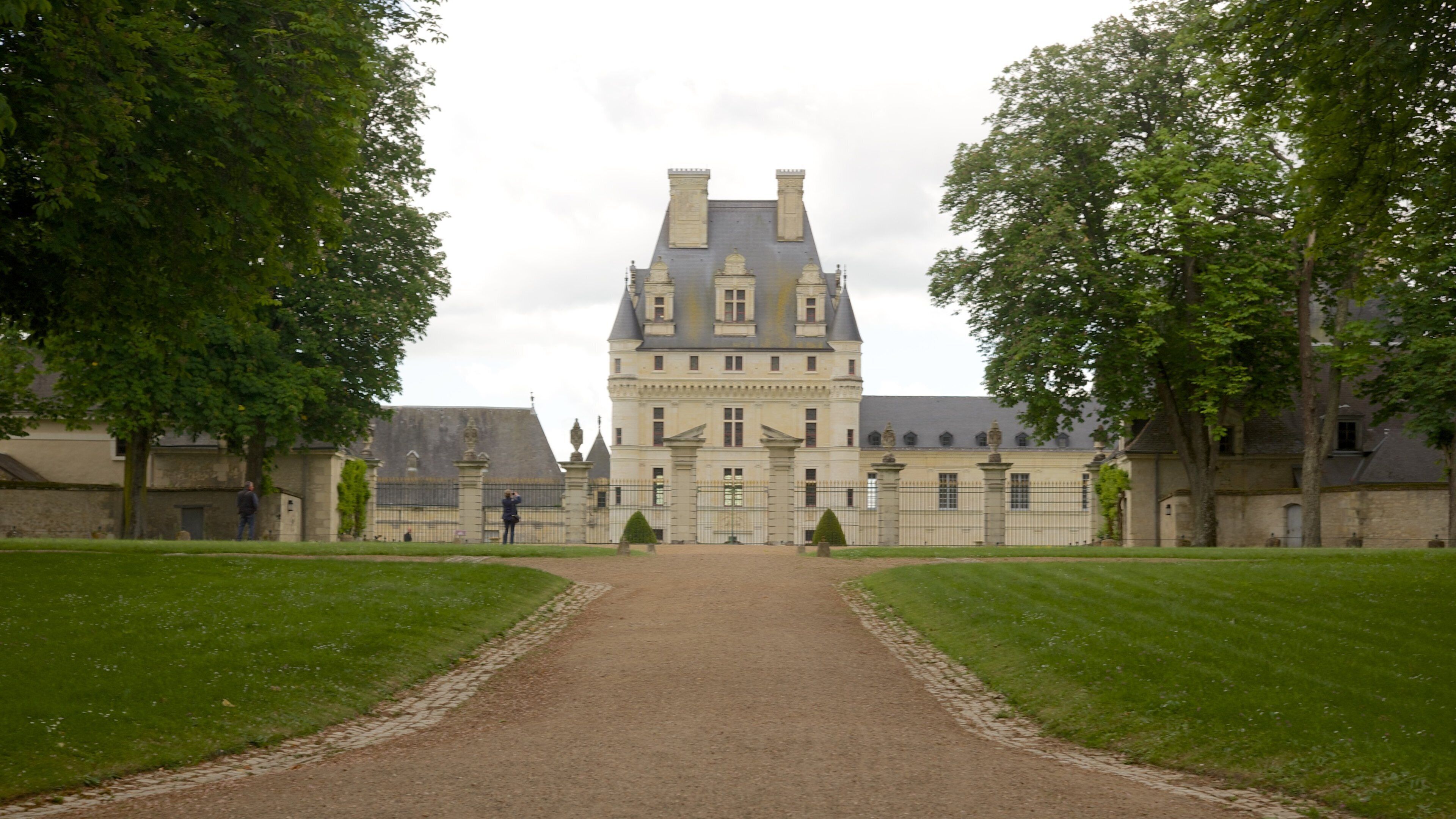 A large, historic building with a symmetrical facade, a central entrance, and a paved pathway leading to it.