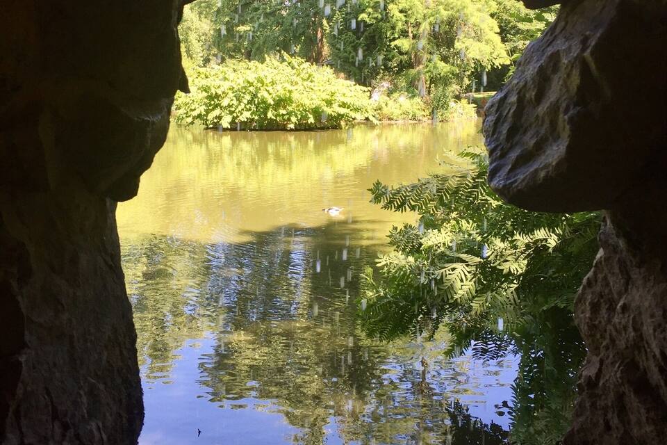 L’entrée d’une grotte, d’où l’on aperçoit un étang bordé d’une végétation luxuriante.