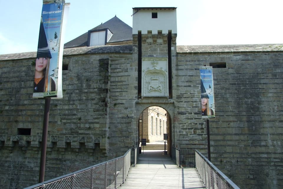 Un pont de pierre menant à un bâtiment historique, orné de bannières et d’un blason.