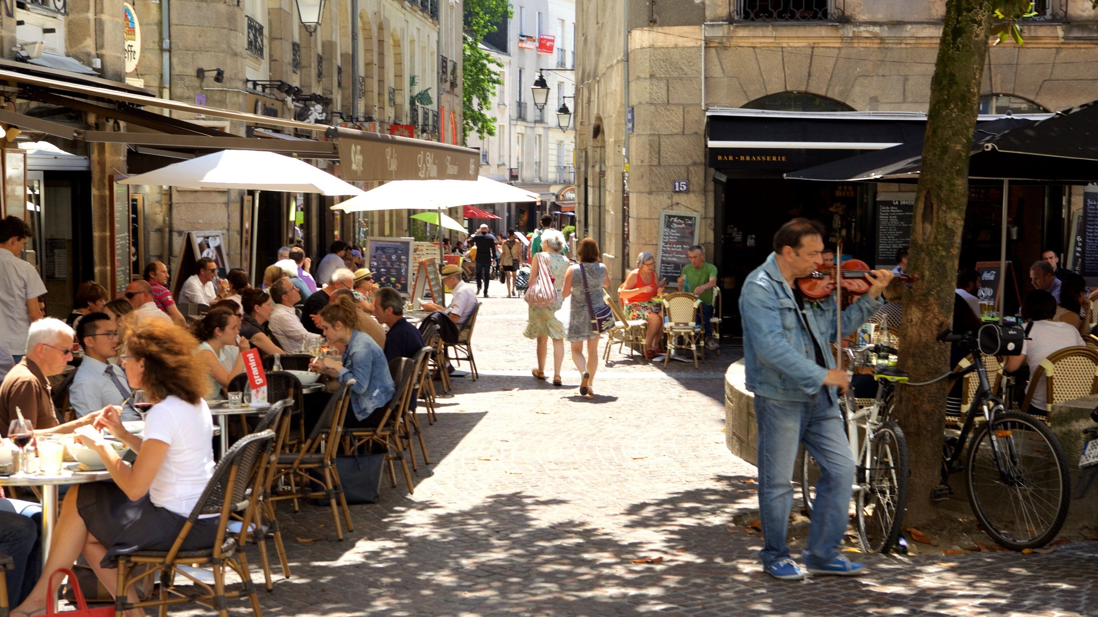A bustling outdoor café with people dining and a musician playing violin.